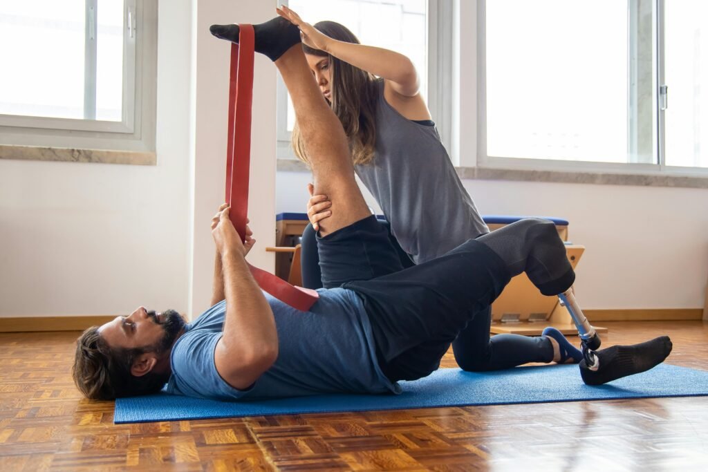 Physical therapist guiding a male patient with a prosthetic leg through stretching and resistance training during a post-surgical recovery session.